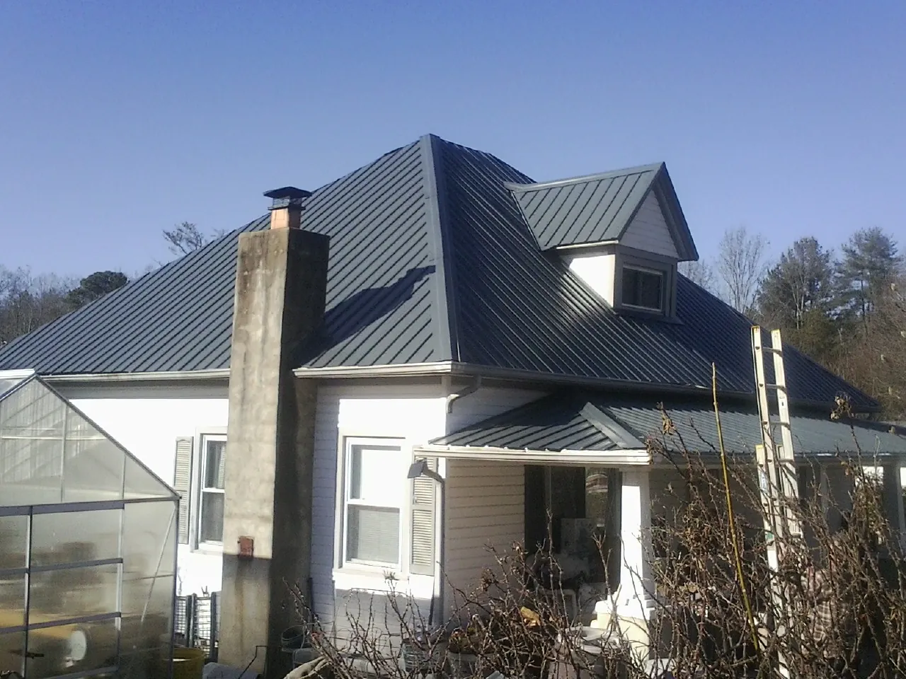 Dark blue standing seam metal roof on a white farmhouse with dormer — Slate & Tile Roof Repair by Roofing Brothers in Withams