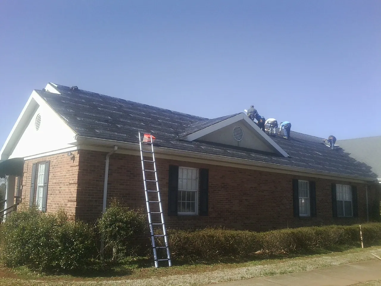 Crew tearing shingles off a brick ranch roof with a ladder set — Emergency Roof Repair work by our crew in Withams