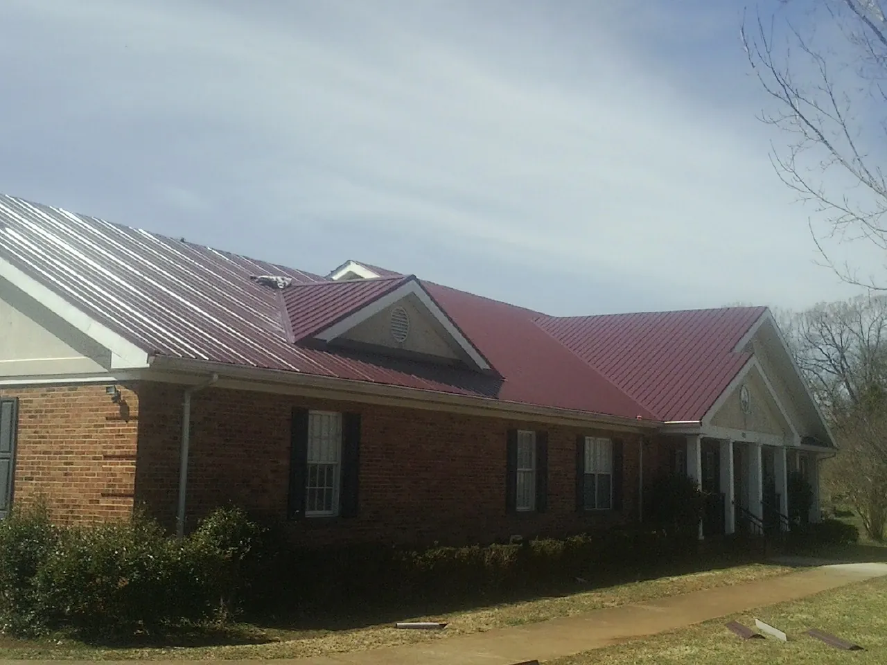 Red metal roof with gabled entries on a long brick building, from a Hail Damage Roof Repair job in Withams