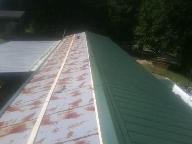 Old rusted panels beside newly installed green metal roofing — Wind Damage Roof Repair by Roofing Brothers in Withams